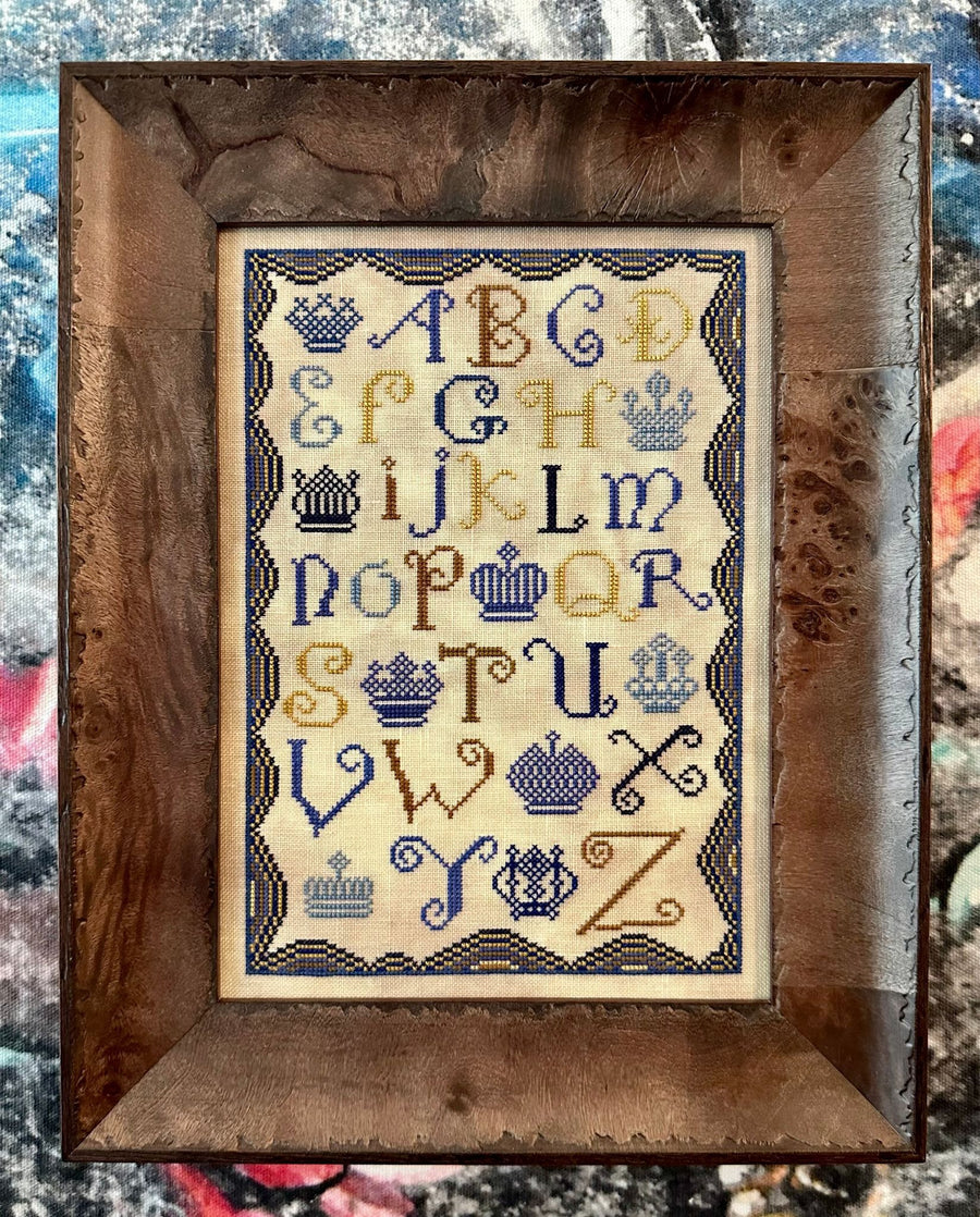 Framed cross-stitched alphabet with decorative elements on a textured background