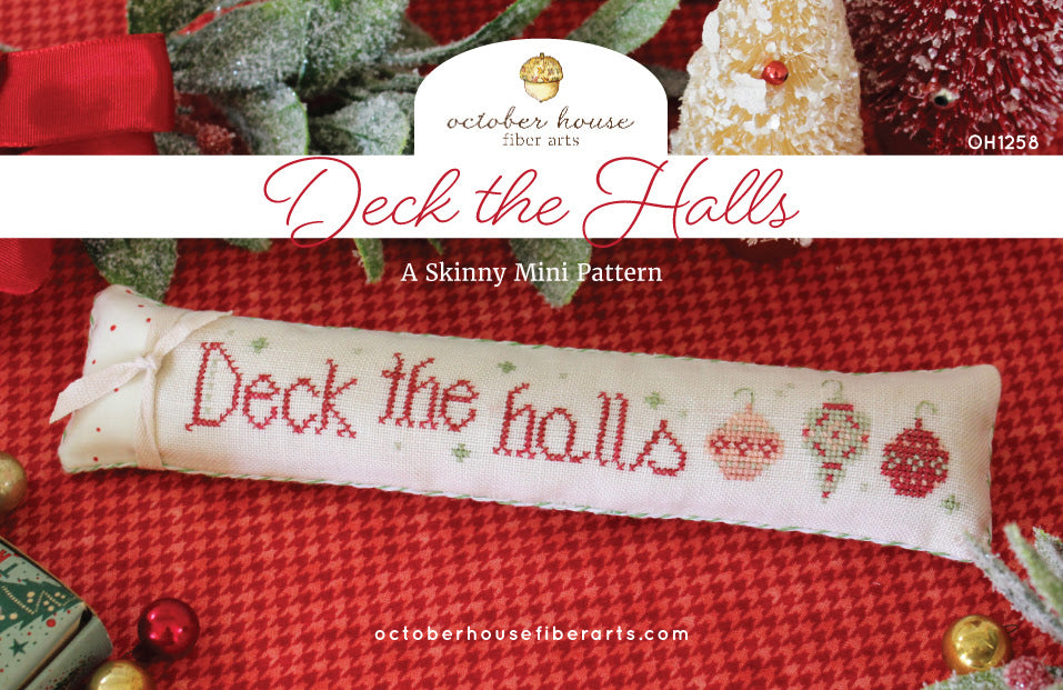 Cross-stitched Skinny Mini pattern with 'Deck the Halls' text on a red fabric background, featuring October House Fiber Arts branding.