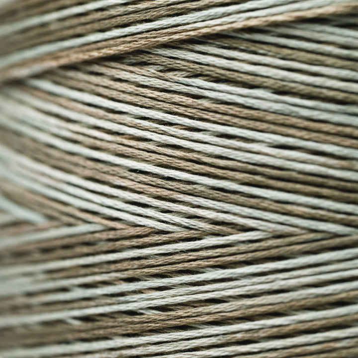 A close-up of tightly wound yarn strands in a heathered mix of taupe, light brown, and off-white.