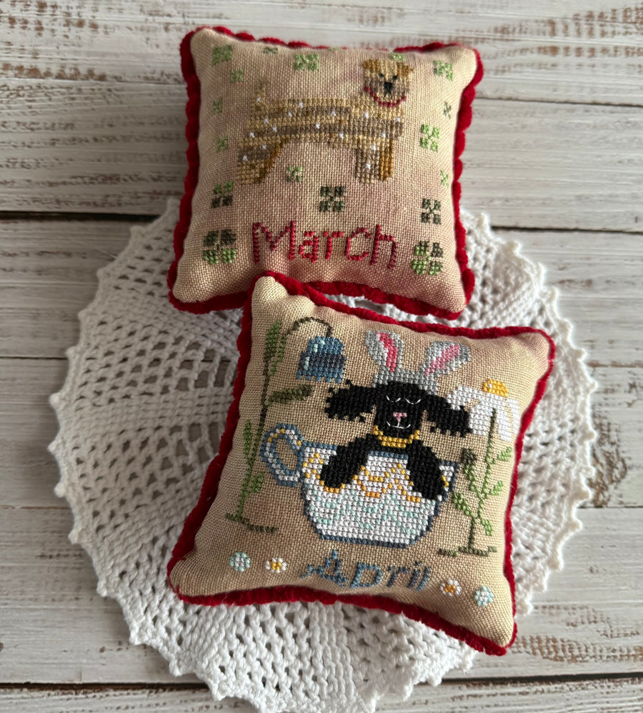 Two cross-stitched pillows with animal designs on a wooden surface.