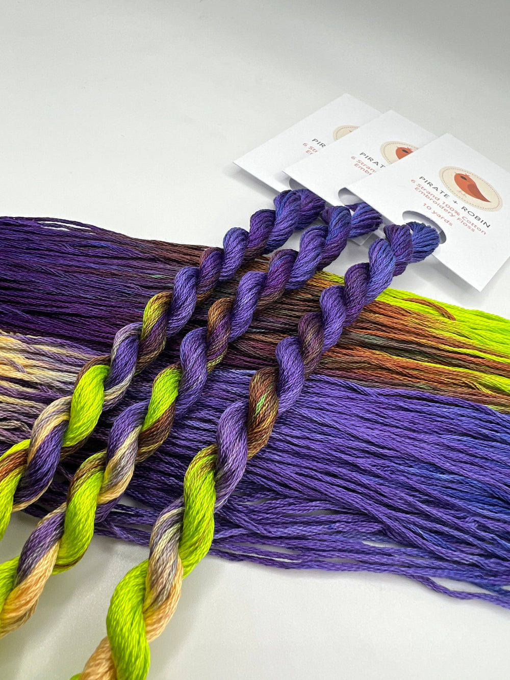 Purple and multicolored thread skeins and strands on a white background with product tags.