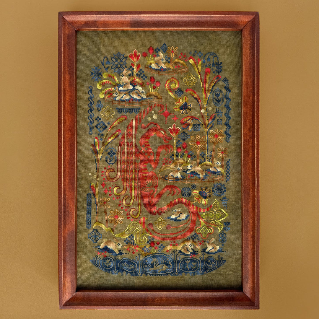 Framed embroidered artwork with intricate designs on a beige background