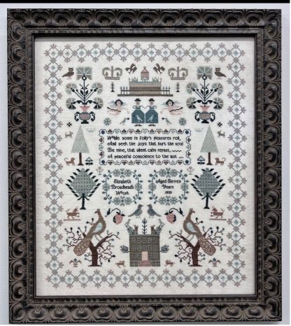 Decorative cross-stitch pattern with intricate designs and text, framed in an ornate black frame.