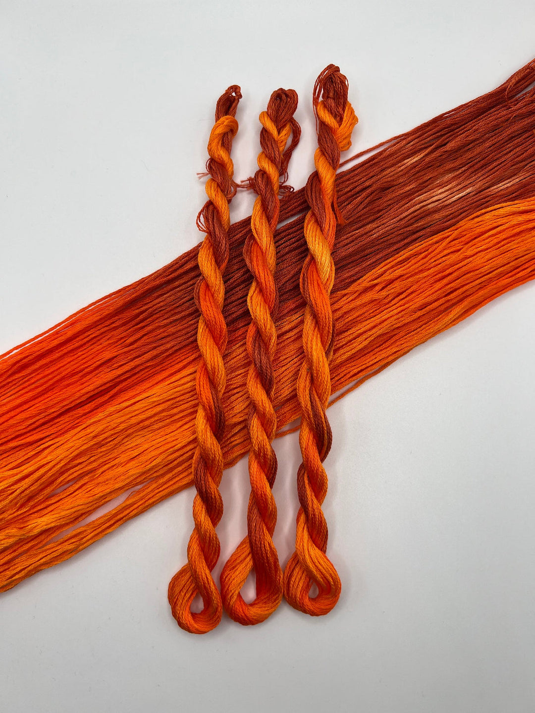 Three braided strands of orange thread on a white background