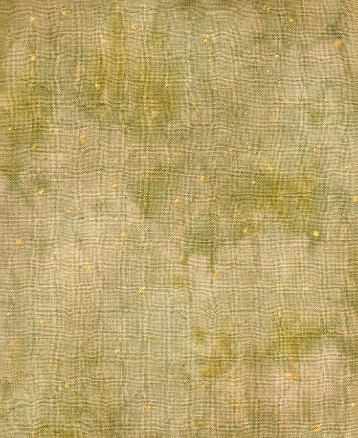 A close-up of a textured fabric with a mottled, watercolor-like pattern in muted olive green, beige, and soft brown, accented with tiny scattered gold flecks.