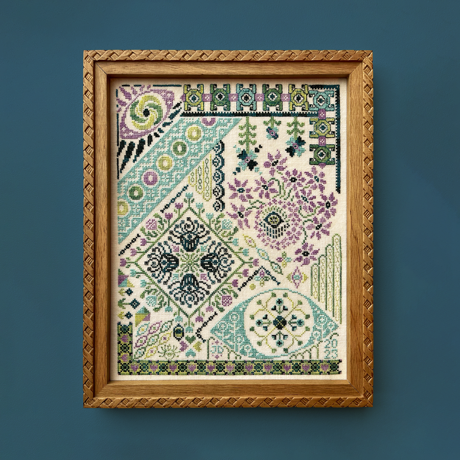 Framed cross-stitched pattern with geometric and floral designs on a blue background