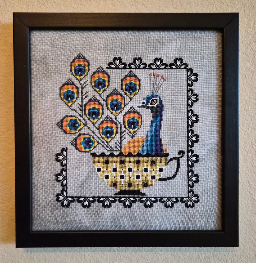Framed cross-stitched peacock design on fabric