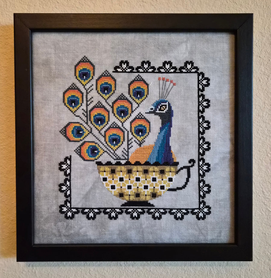 Framed cross-stitched peacock design on fabric