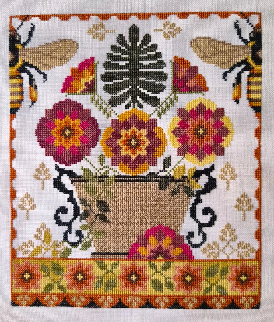 Cross-stitched design with flowers, bees, and a basket on a white background