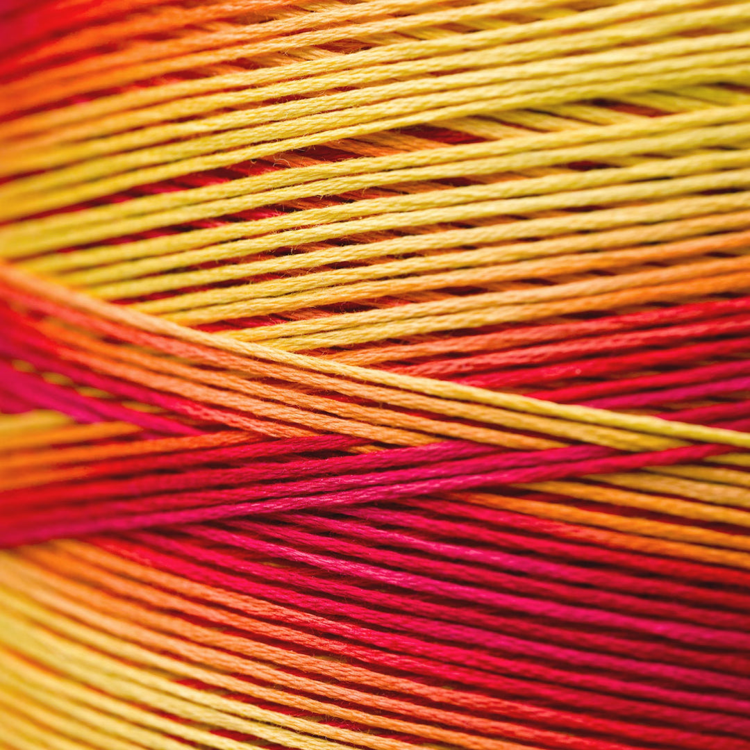 Close-up of a skein of variegated thread with a warm gradient transitioning from golden yellow to orange and deep red.