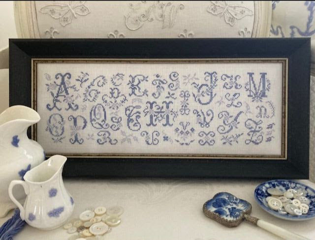 Framed cross-stitched alphabet pattern with decorative items on a surface