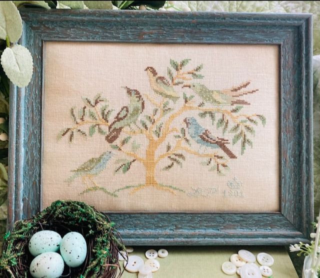 Framed cross-stitched artwork of birds on a branch with a nest and eggs in front