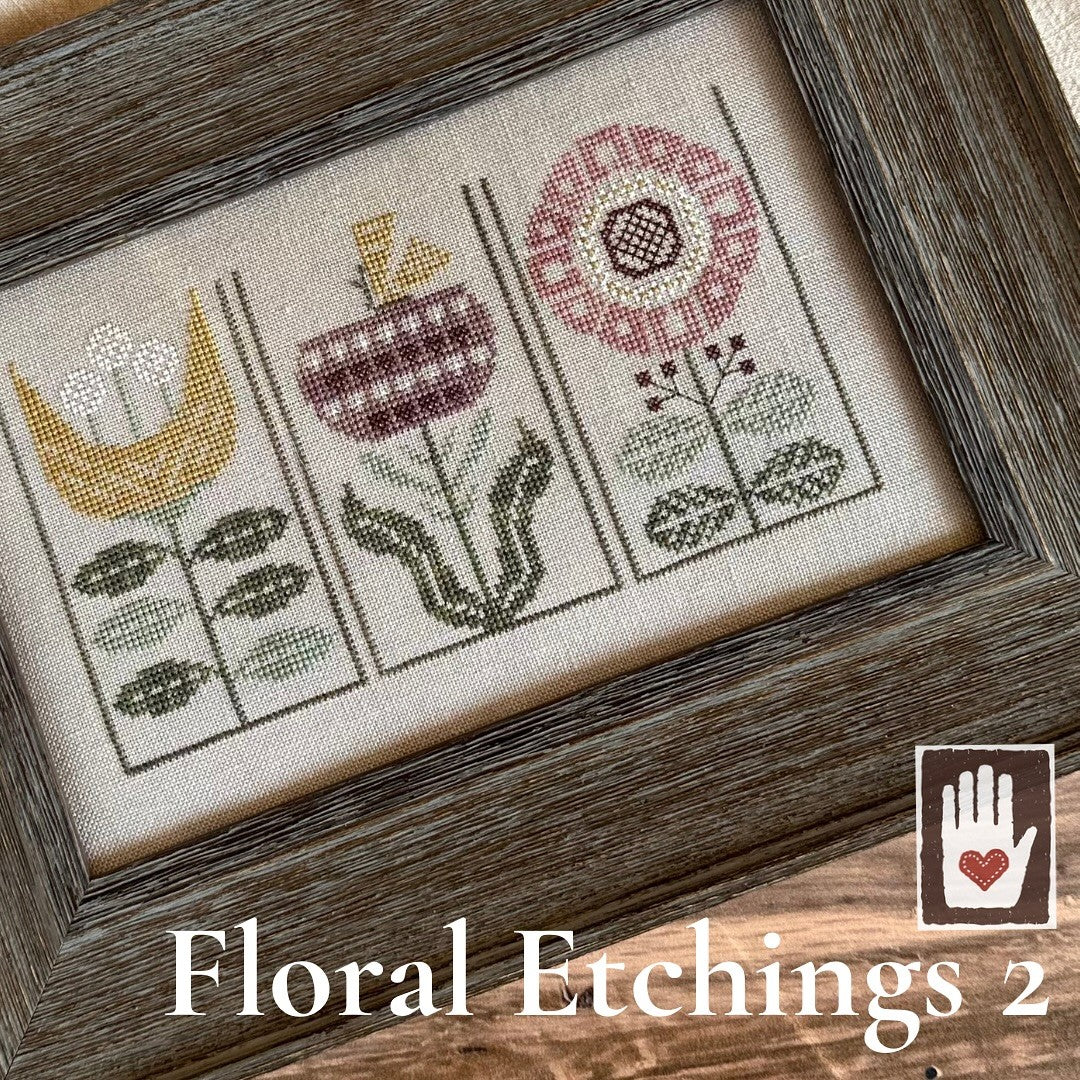 Floral cross-stitch design with a wooden frame on a wooden surface, labeled 'Floral Etchings 2'.