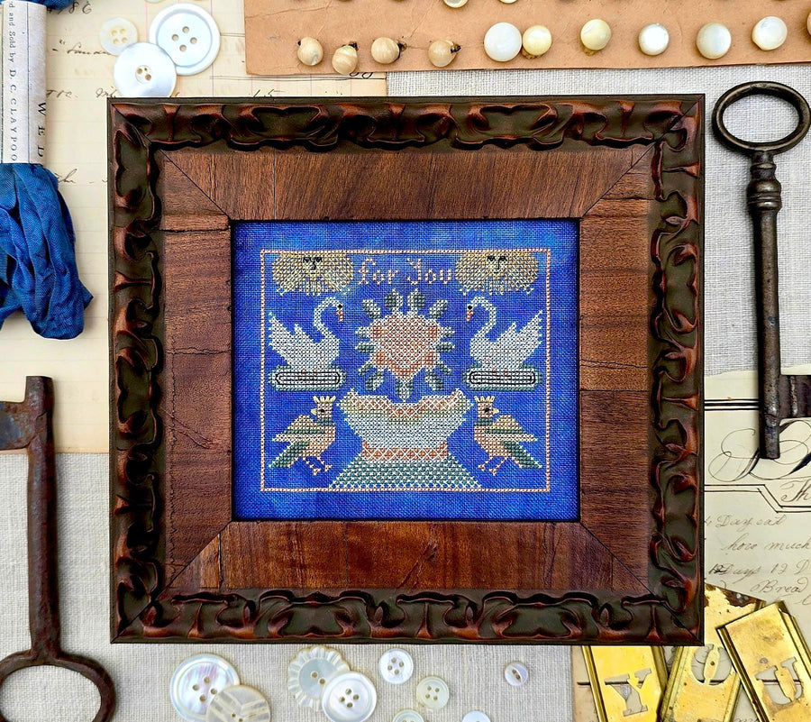 Framed cross-stitched artwork with decorative elements on a textured surface