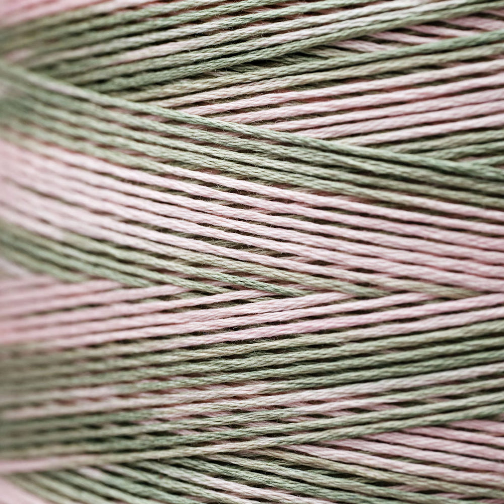 Close-up of twisted yarn strands in a variegated pattern of dusty sage green and soft blush pink.