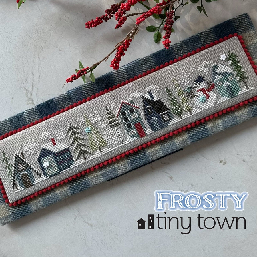Cross-stitched panel of a snowy village with 'Frosty Tiny Town' text on a textured surface.