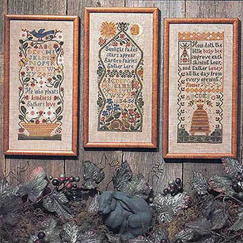 Three framed cross-stitched pieces on a wooden surface with decorative elements.