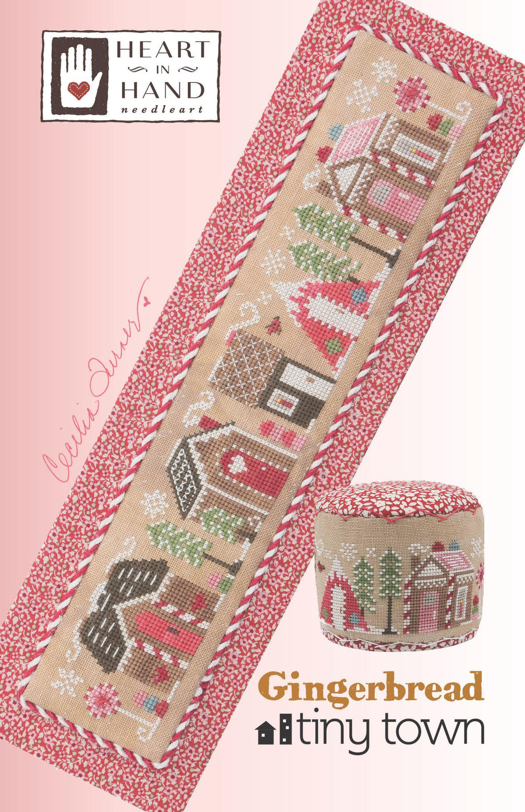 A needlework pattern or kit cover showing a cross-stitch design titled 'Gingerbread tiny town' by Heart in Hand Needlework. The design features a long rectangular sampler and a matching cylindrical pillow, both decorated with a winter village scene in pink, red, green, and brown on a beige background, surrounded by a red-and-white patterned border.