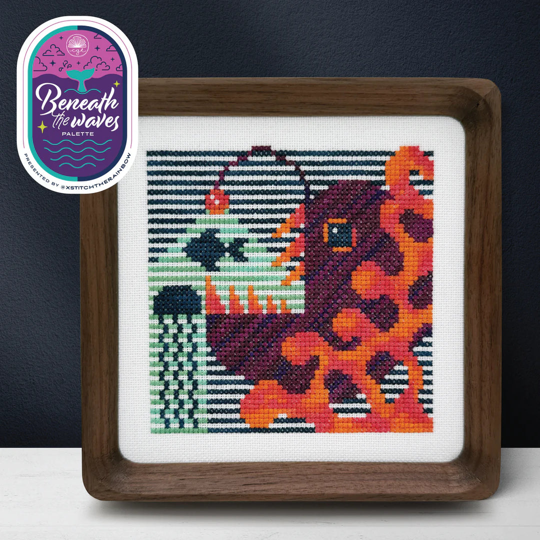 Framed cross-stitched artwork of a colorful abstract design with 'Beneath the Waves' label.