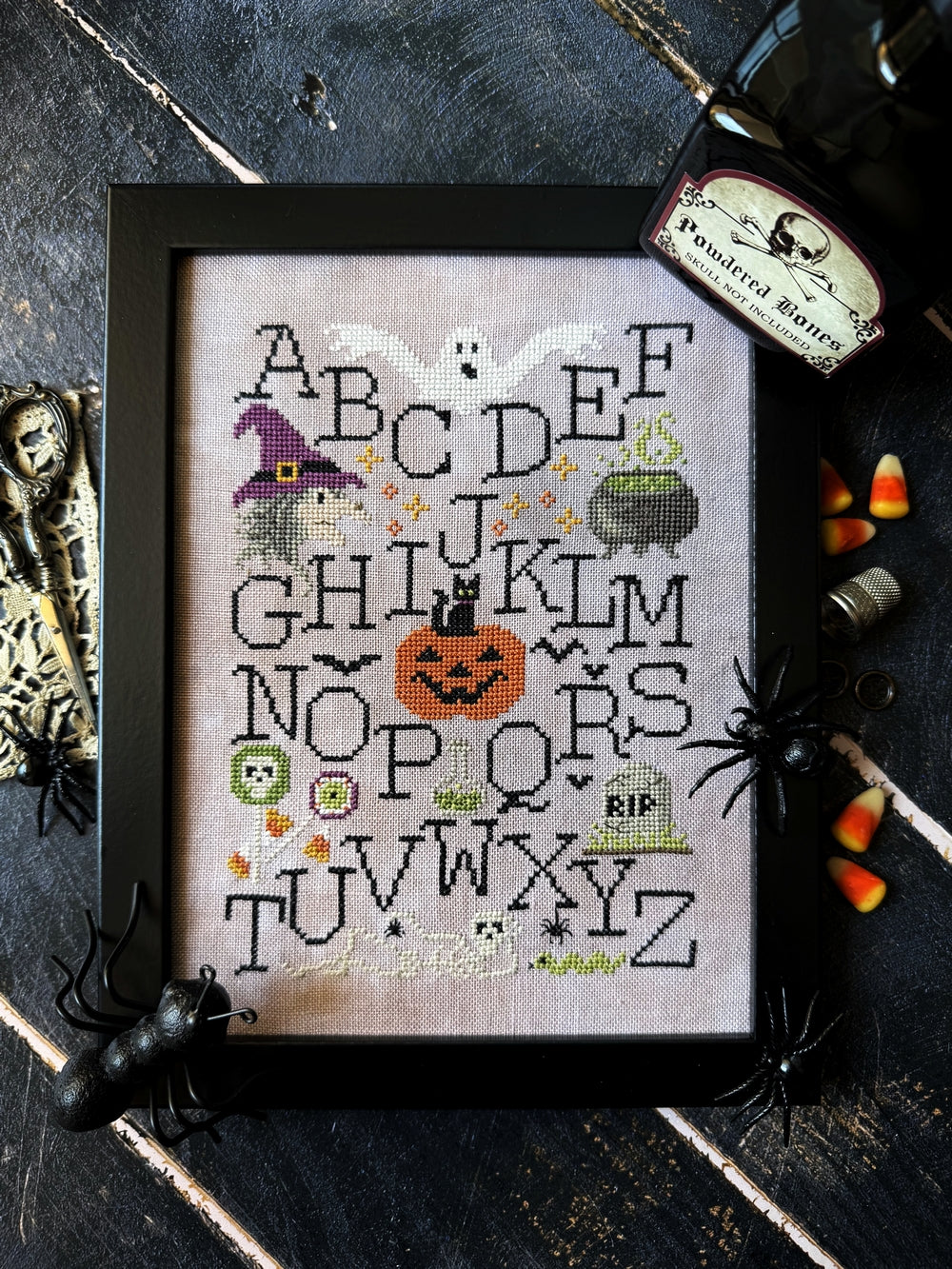 Halloween-themed cross-stitched alphabet with decorative elements on a dark background.