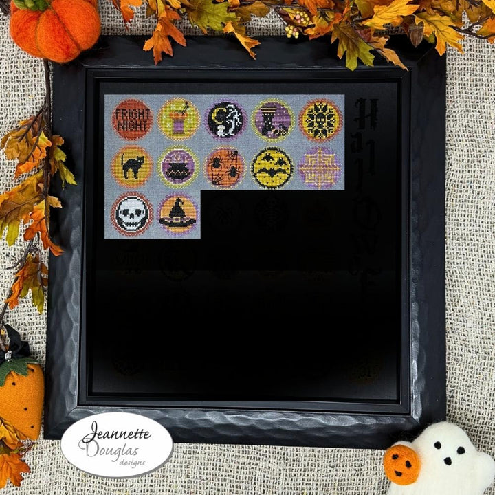 Framed cross-stitch pattern with Halloween-themed designs on a textured fabric background.
