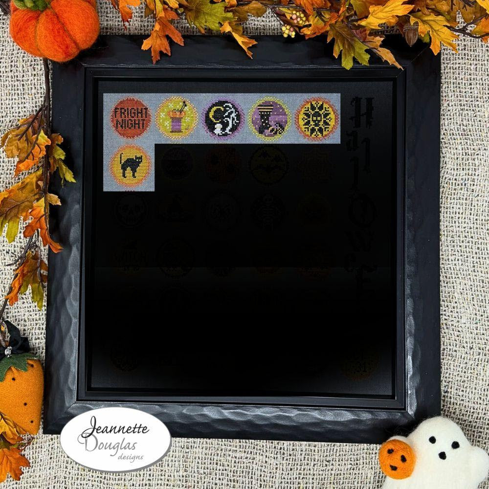 Framed cross-stitched Halloween-themed designs with decorative pumpkins and leaves on a textured fabric background.