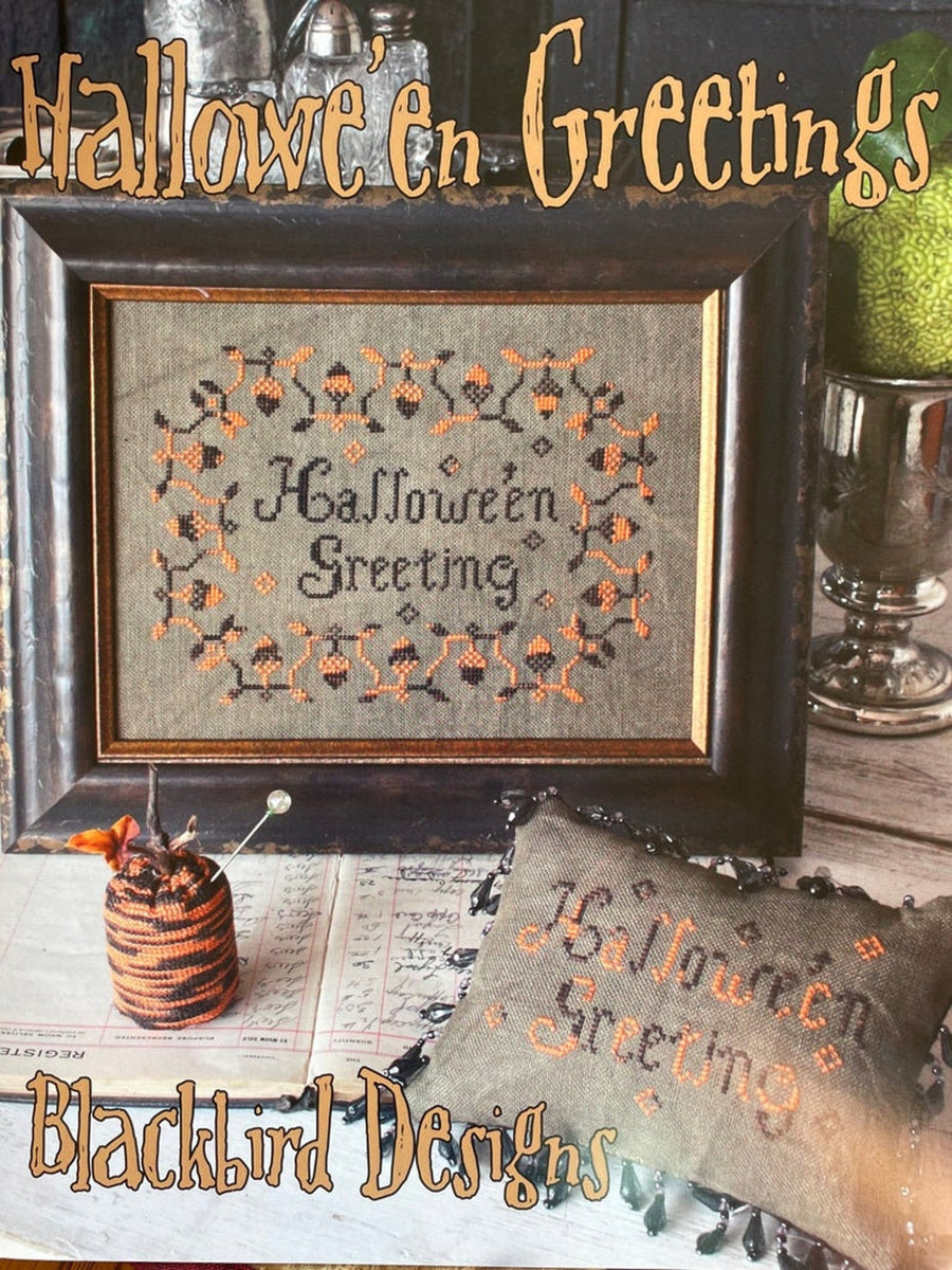 Framed Halloween-themed cross-stitch design with 'Halloween Greetings' text, surrounded by decorative items.