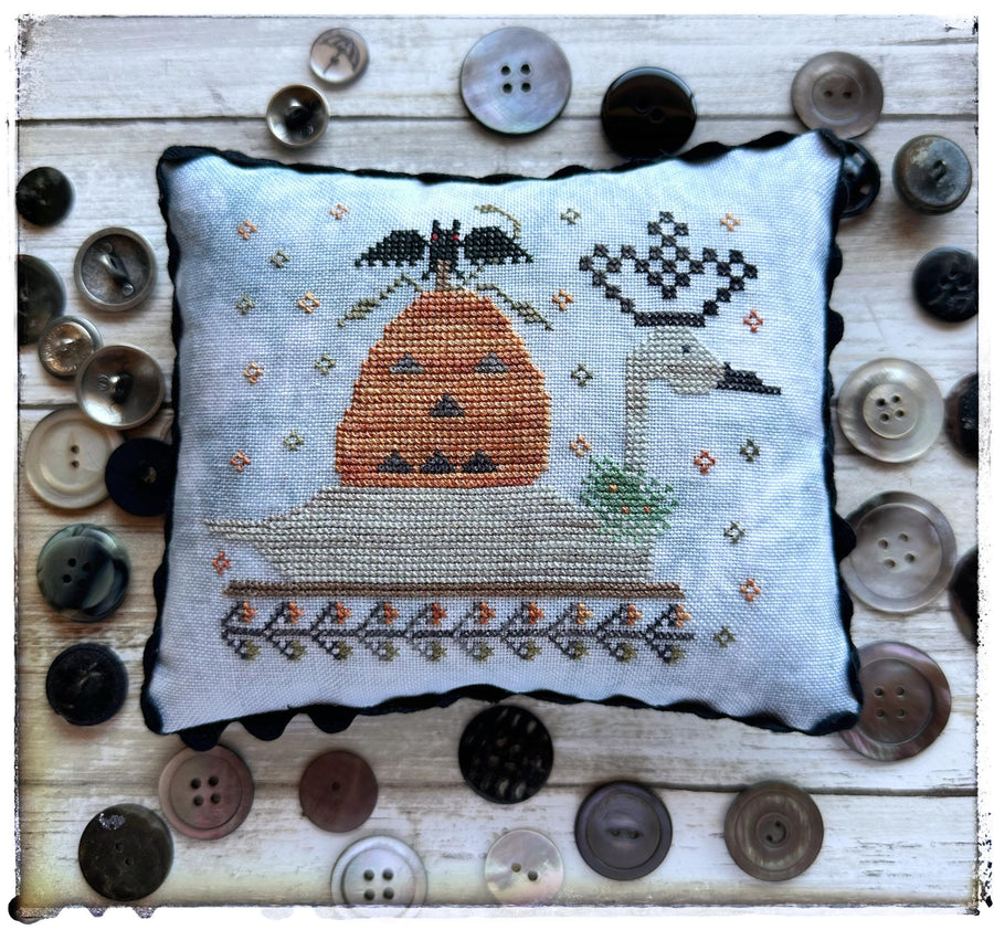 Cross-stitched pillow with a bird design on a wooden surface with buttons.
