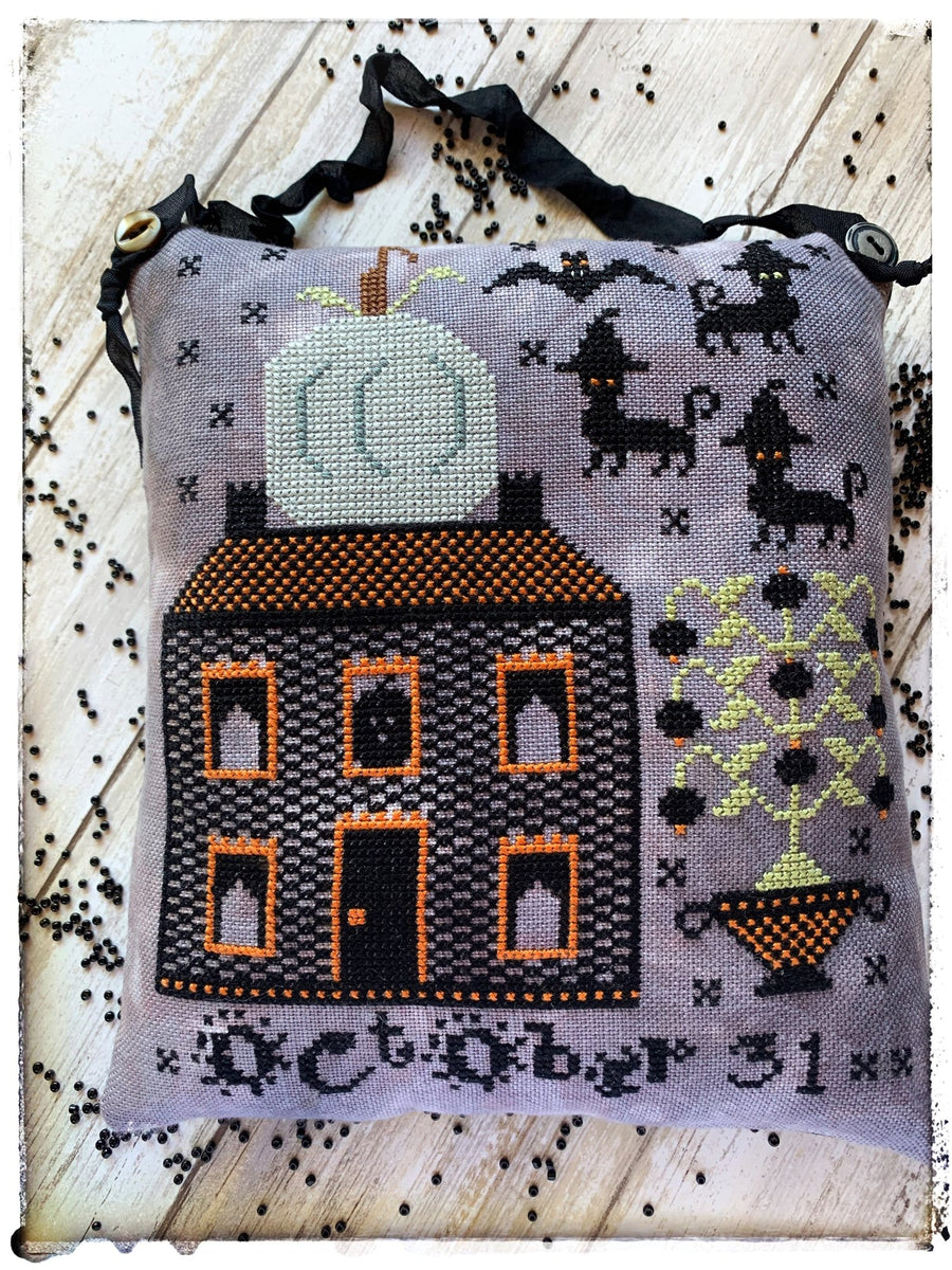 Cross-stitched design of a house with a pumpkin on a gray background, featuring Halloween-themed elements.