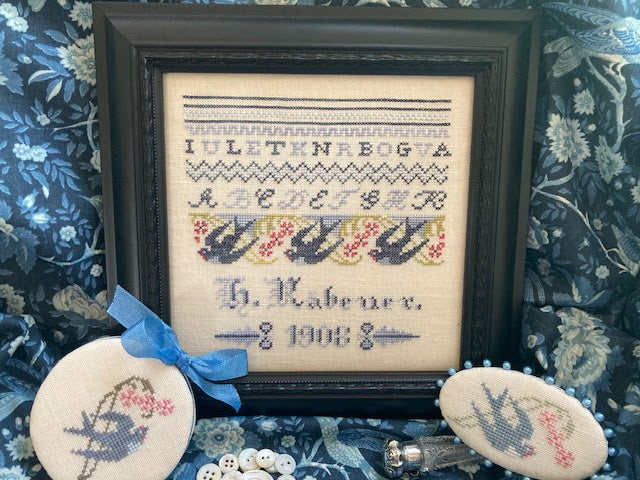 Framed cross-stitched sampler with decorative stones on a floral fabric background