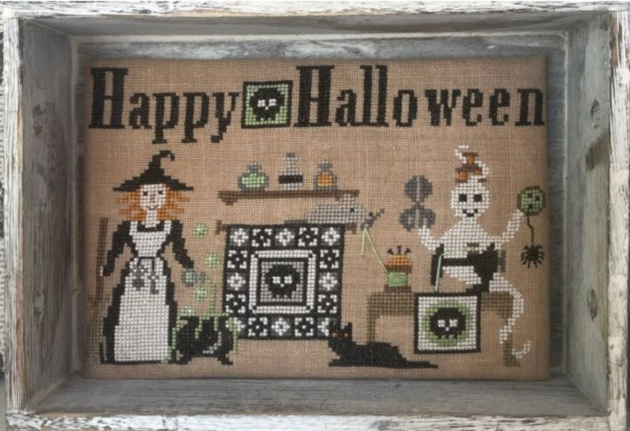 Halloween-themed cross-stitched design with a witch, skeleton, and cat on burlap fabric.