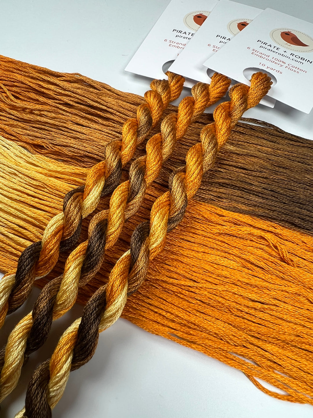 Three skeins of brown and orange embroidery floss with matching color swatches on a white background.