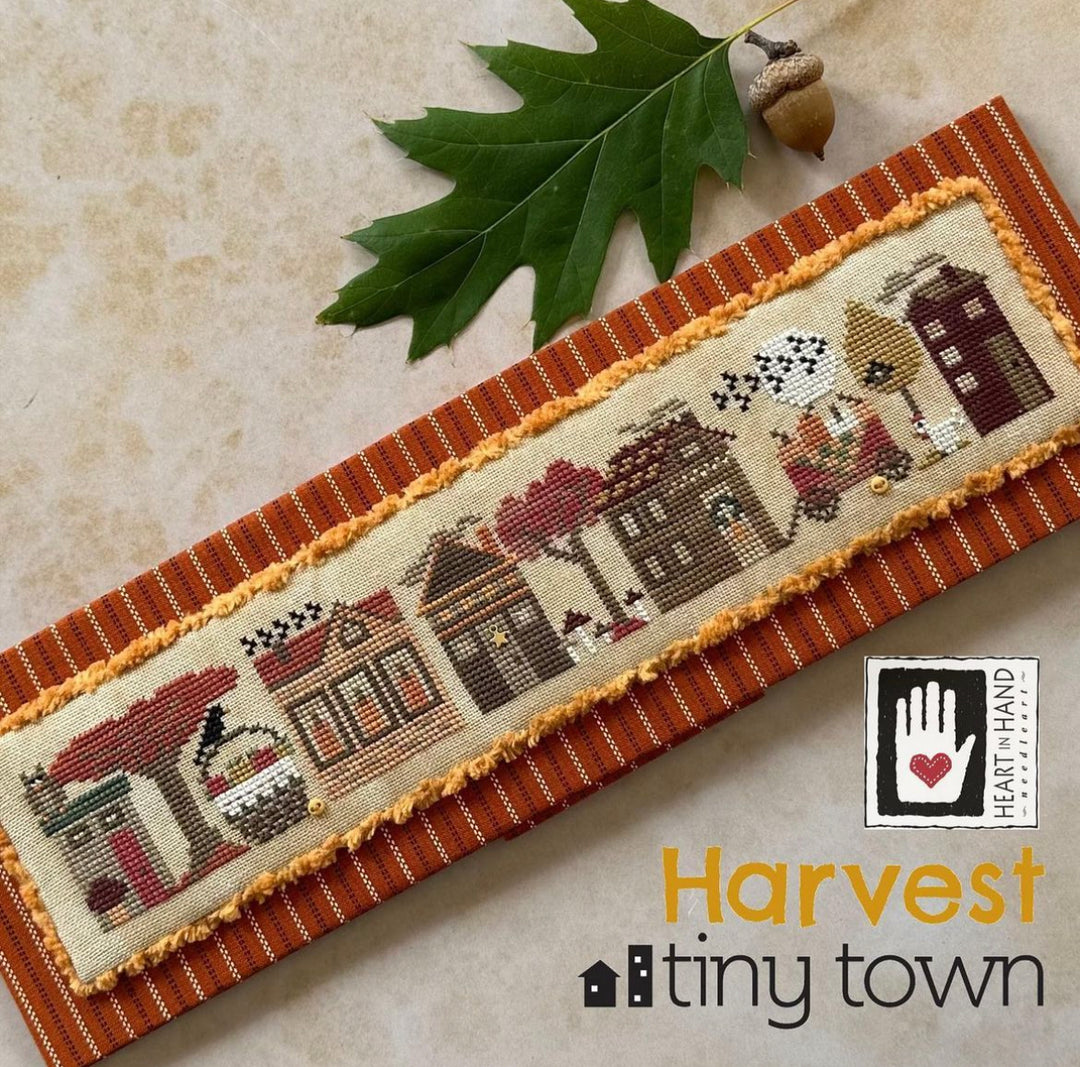 Cross-stitched panel with autumn-themed design on a textured surface with an acorn and leaf.