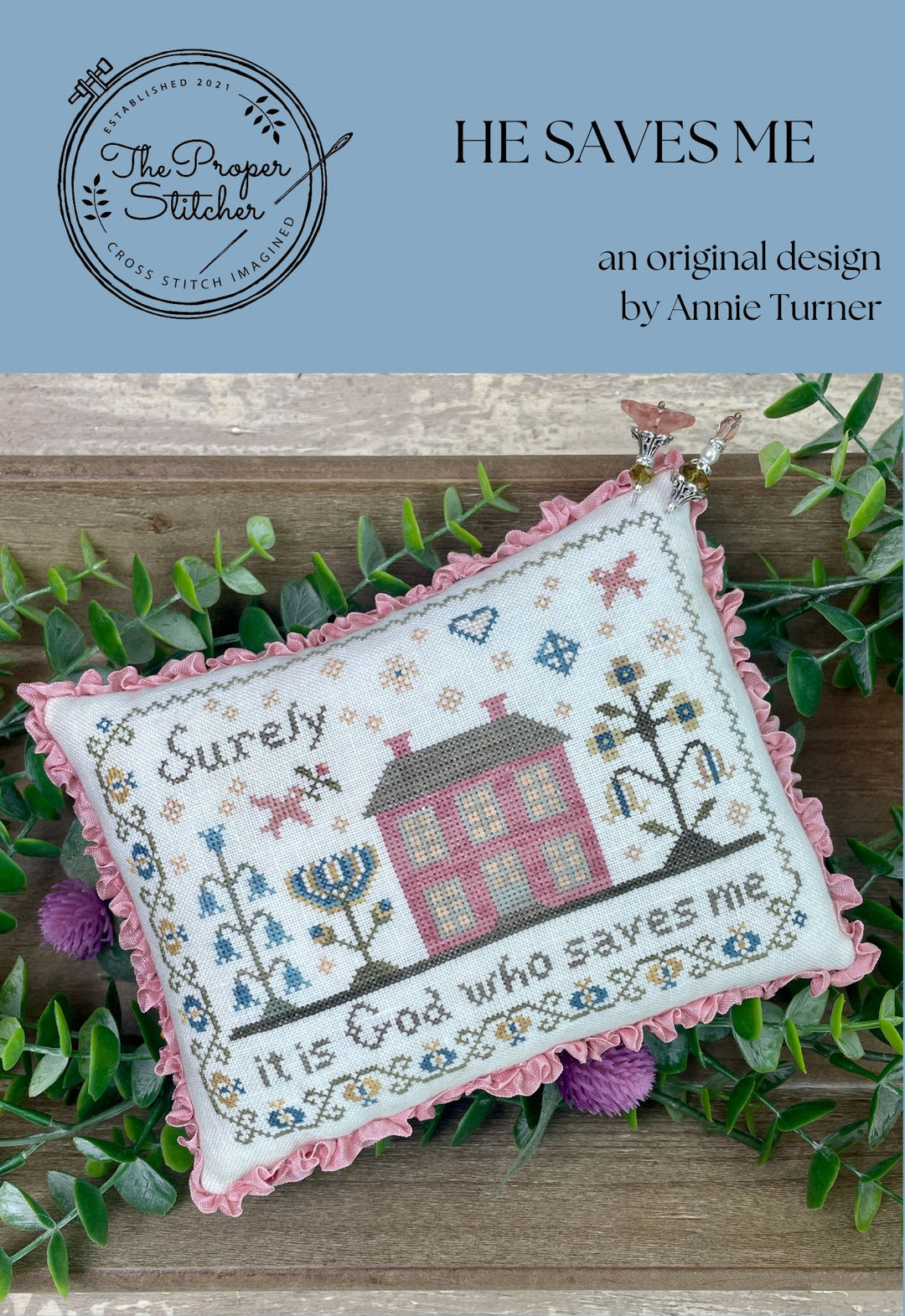 Cross-stitched pillow with decorative elements on a wooden surface with greenery