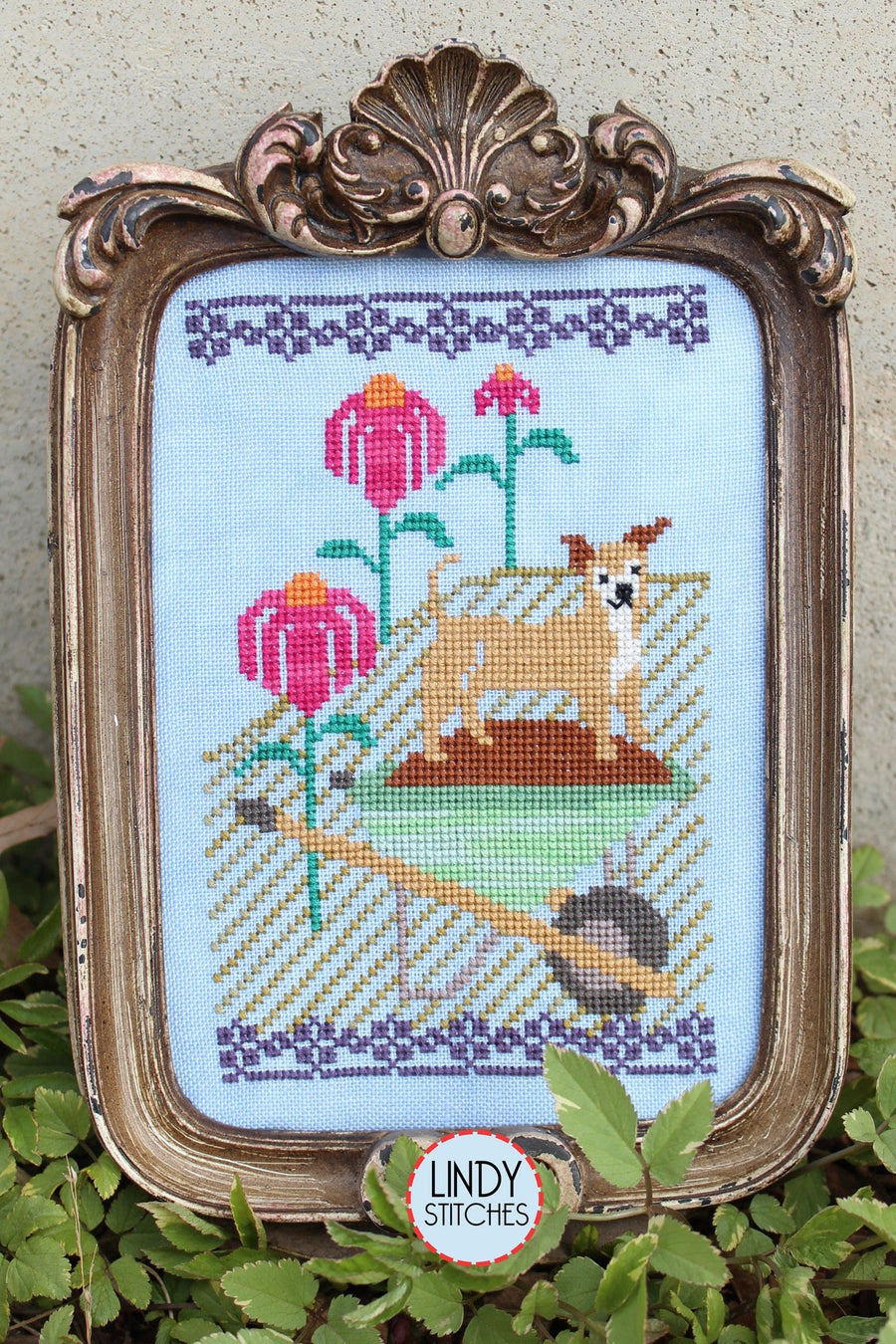 Framed cross-stitched piece with a dog and flowers, featuring Lindy Stitches branding.
