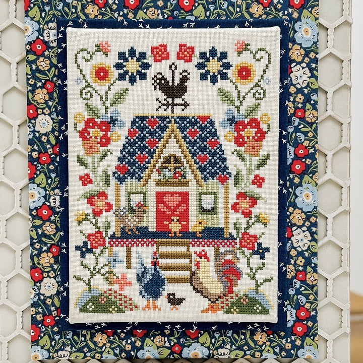 Decorative cross-stitch pattern with a chicken coop and flowers on a white background.