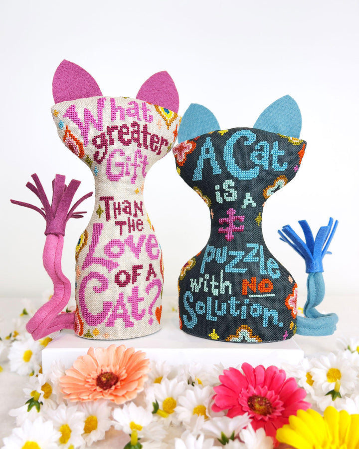 Two decorative cat-shaped pillows with embroidered text on a white background with flowers.