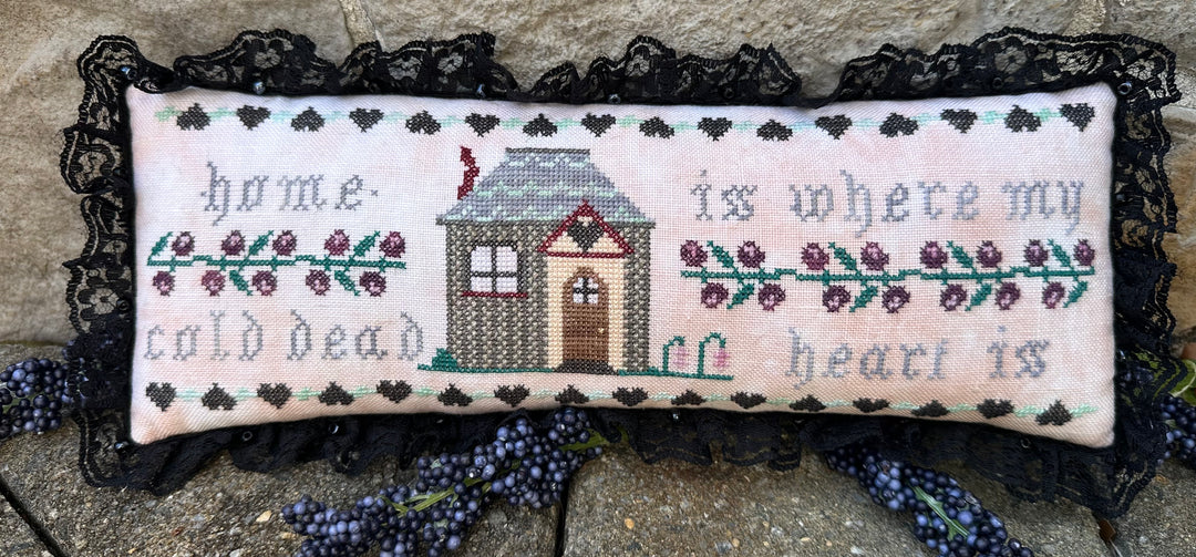 Decorative pillow with cross-stitched text and house design on a lace background