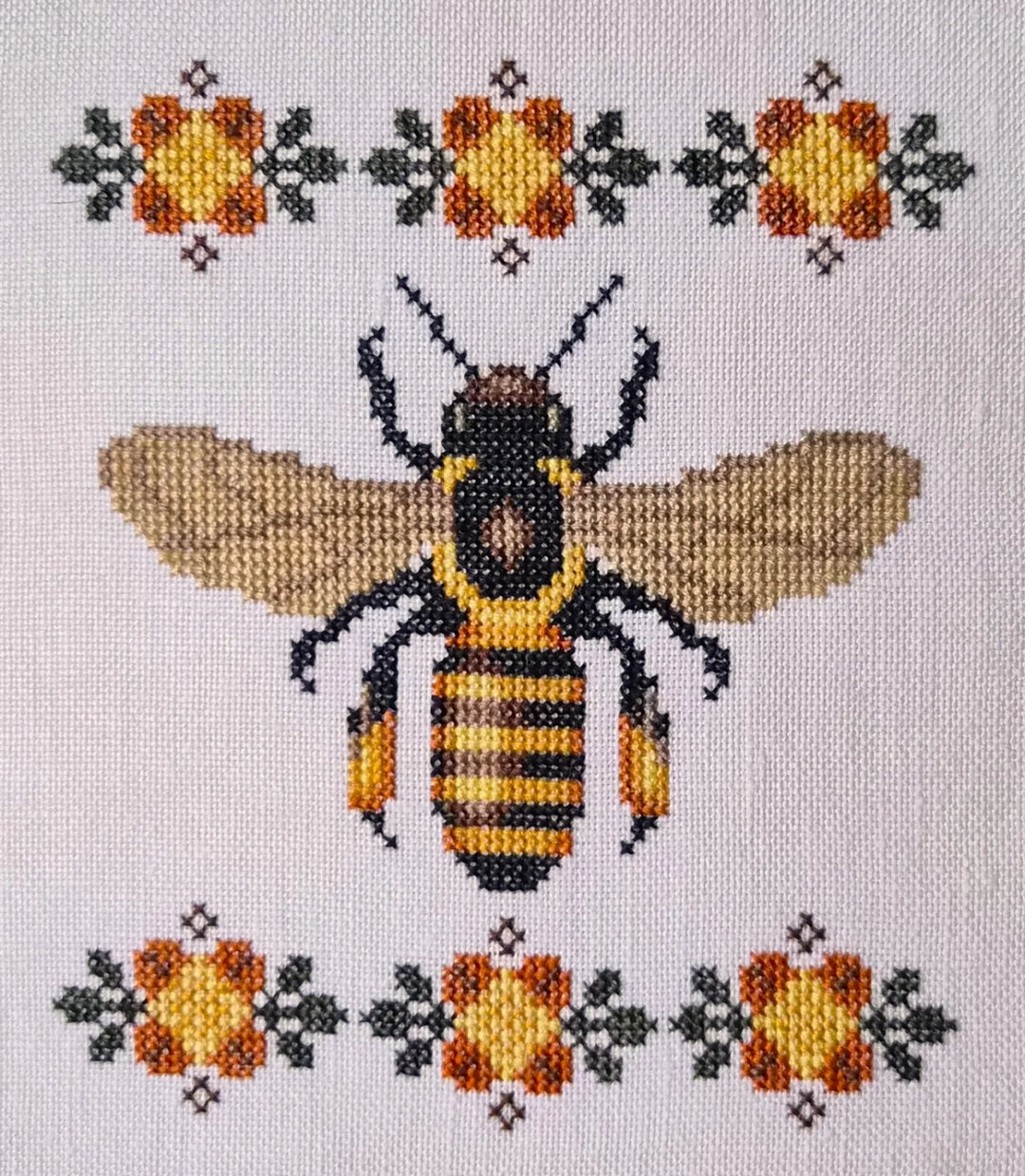 Cross-stitched bee design with floral patterns on a light background