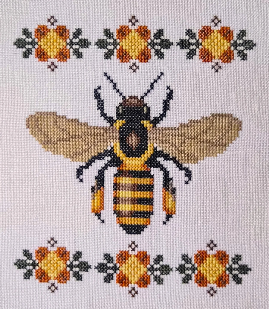 Cross-stitched bee design with floral patterns on a light background