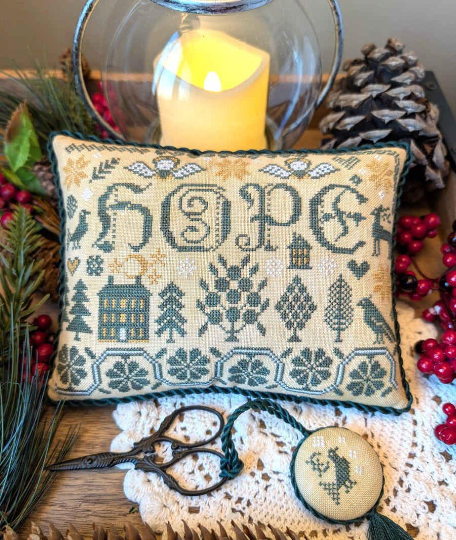 Decorative pillow with 'HOPE' embroidery surrounded by festive elements like pine cones and berries.