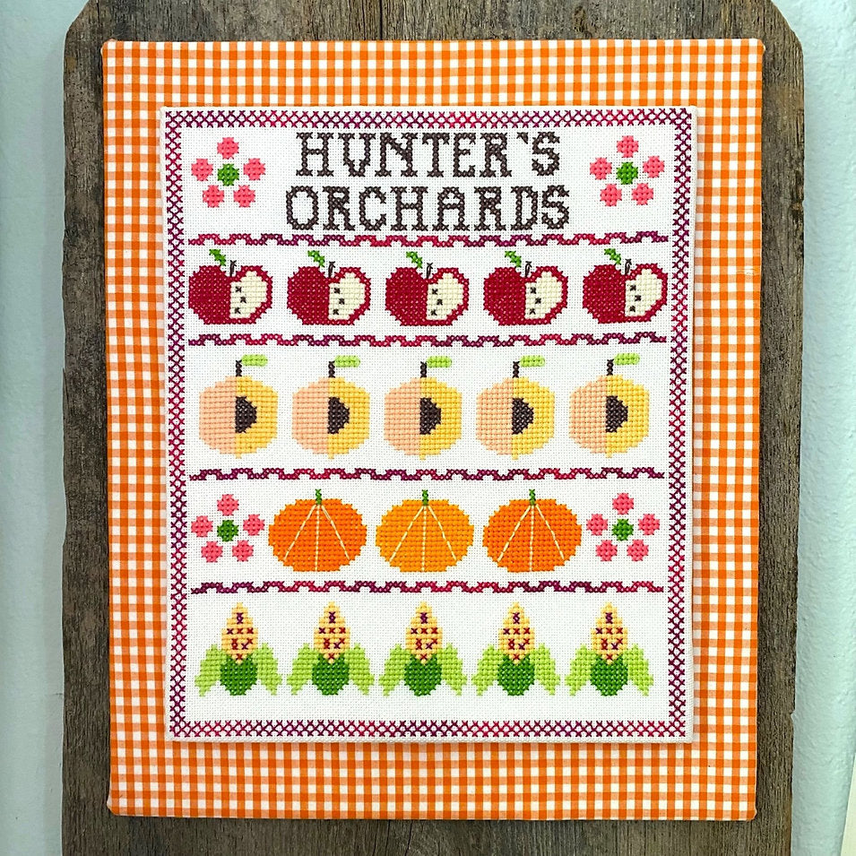 Cross-stitched design of fruits and vegetables on a checkered fabric background