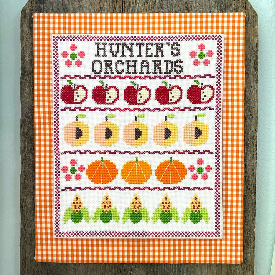 Cross-stitched design of fruits and vegetables on a checkered fabric background