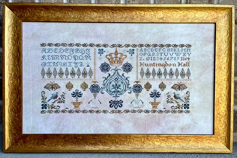 Decorative cross-stitch pattern with alphabets, numbers, and symbols in a gold frame.