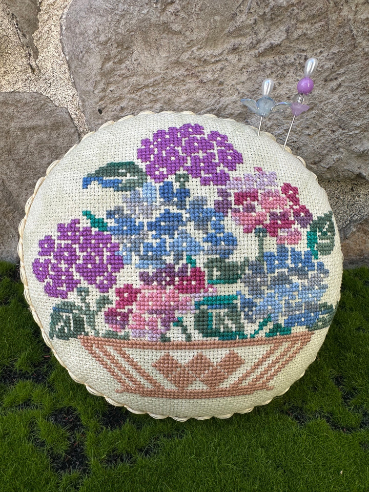 Round cros stitched pillow with floral pattern on a stone surface