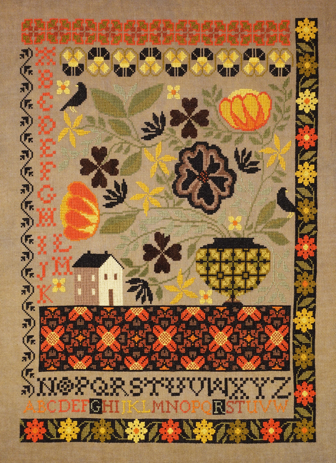 Decorative cross-stitch pattern with flowers, pumpkins, and a house on a beige background.