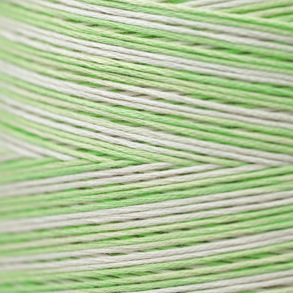 A close-up of light green and off-white yarn strands wound together, showing the texture and color pattern.