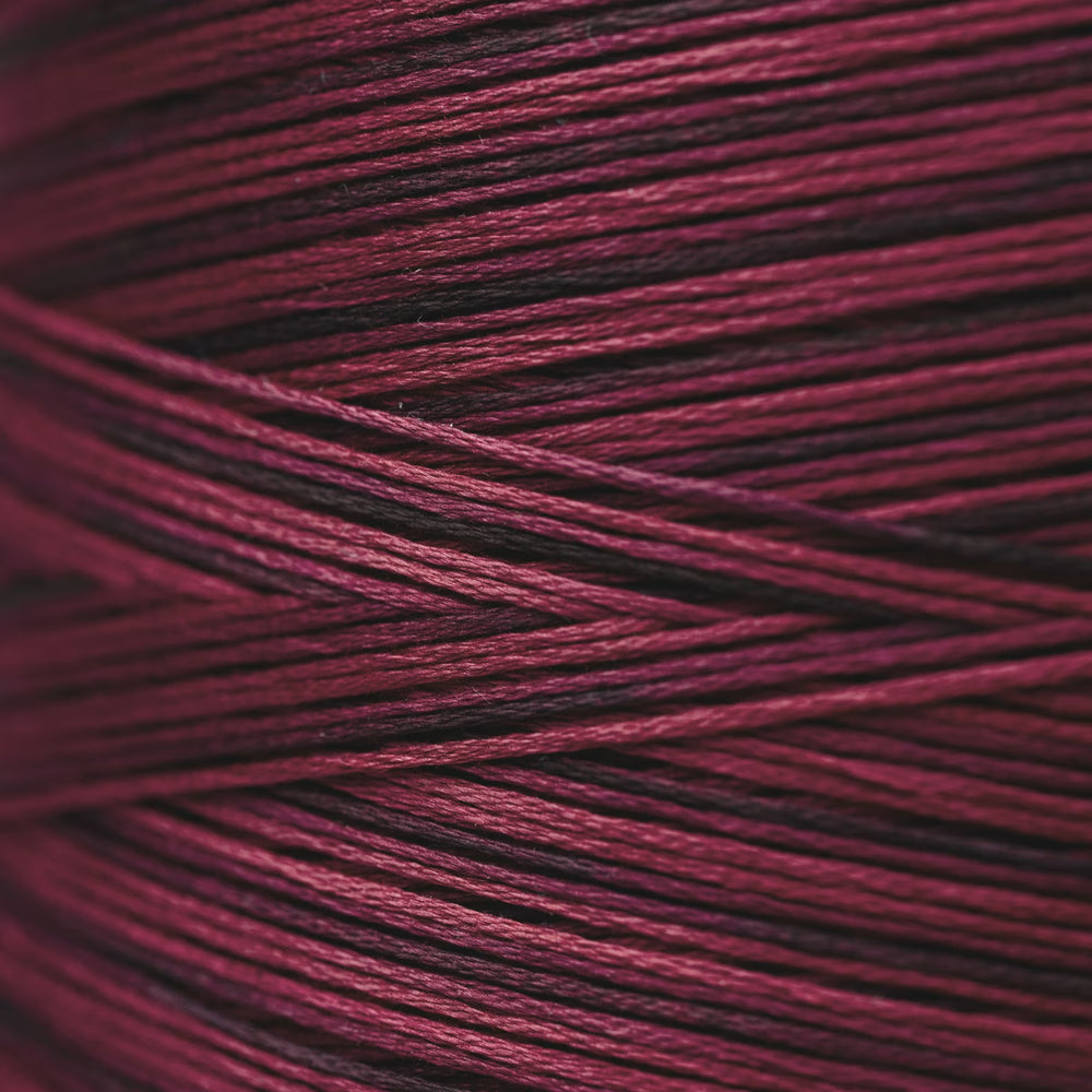 A close-up of tightly wound yarn strands in a deep wine and burgundy tone, filling the entire frame.