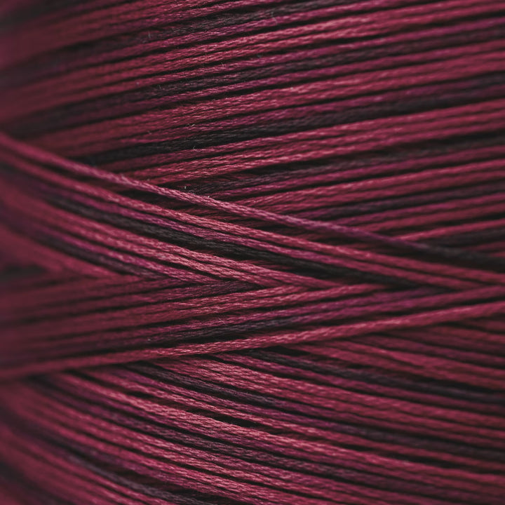 A close-up of tightly wound yarn strands in a deep wine and burgundy tone, filling the entire frame.