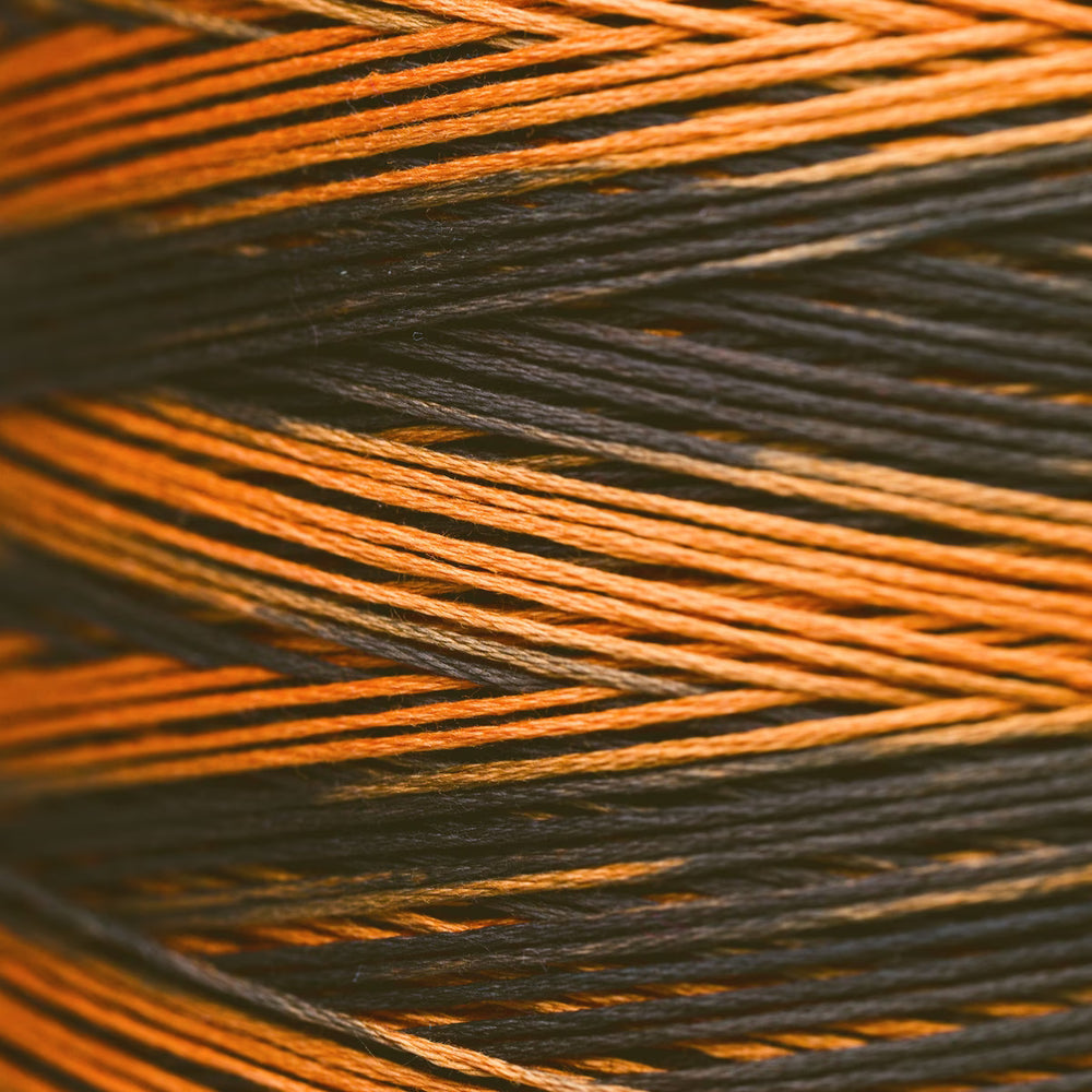 Close-up of tightly wound thread strands in alternating orange and black colors, filling the entire frame.